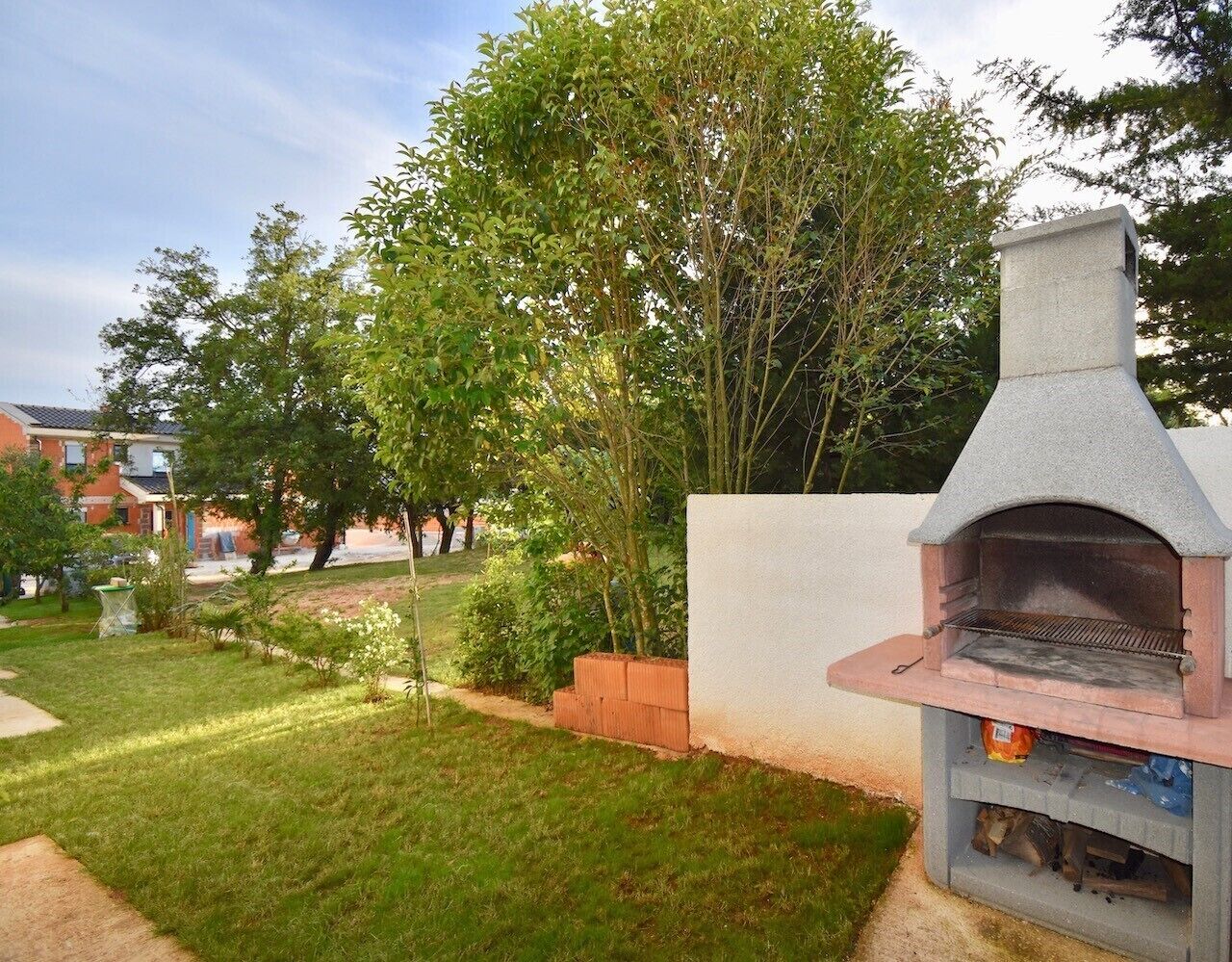 Un jardin avec un barbecue en pierre, une pelouse et un arbre.