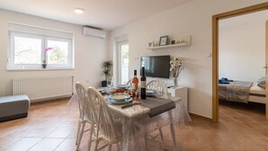 Un comedor con una mesa preparada para dos personas, un televisor montado en la pared y una cama visible a través de una puerta abierta.