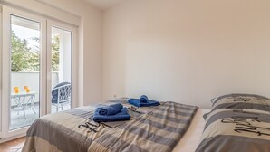 Un dormitorio con una cama, una silla y una mesa con bebidas. Hay una puerta corrediza de vidrio que da a un área exterior.