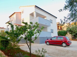 Stylish two-story building with a flat roof and balcony, set amidst a lush garden and a driveway.