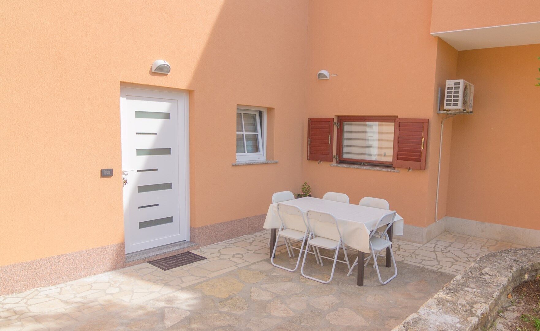 Une terrasse avec une table et des chaises, une porte et une fenêtre avec des volets.