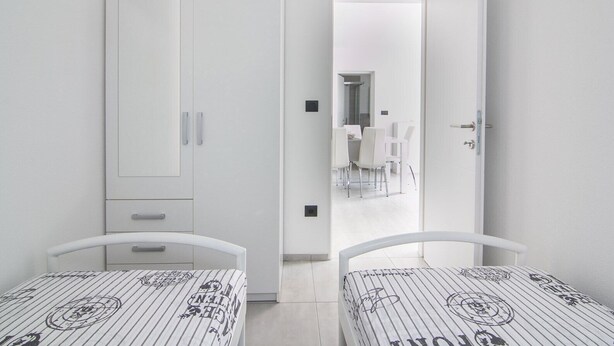 Ein Zimmer mit zwei Einzelbetten, einem Kleiderschrank und einer offenen Tür zu einem Essbereich mit Tisch und Stühlen.