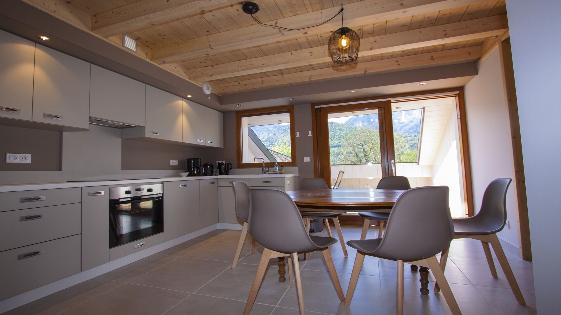 A modern kitchen with grey cabinets, a built-in oven, and a dining area with a wooden table and four chairs.