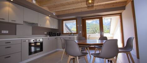 A modern kitchen with grey cabinets, a built-in oven, and a dining area with a wooden table and four chairs.