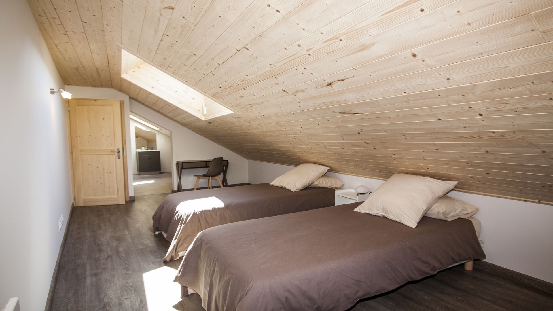 A bedroom with two beds, wooden ceiling, and a skylight.