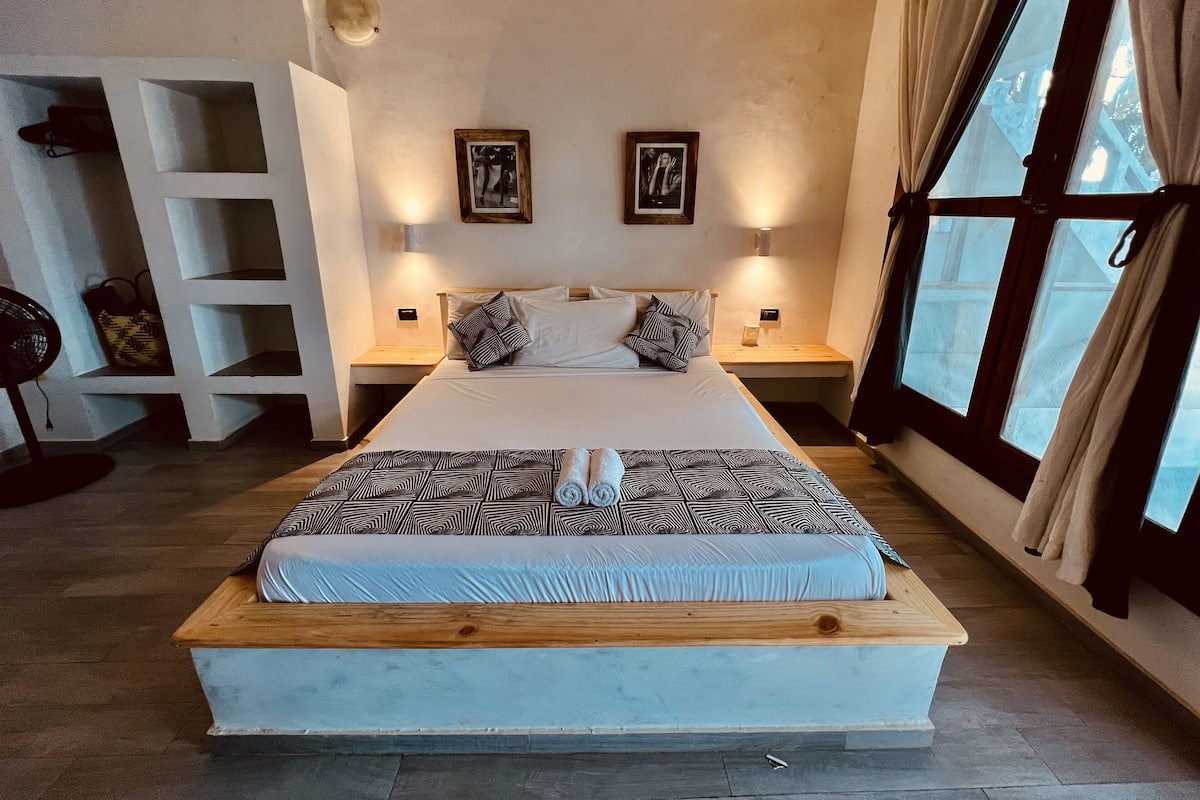 Un dormitorio moderno con una cama grande, dos mesitas de noche, una estantería empotrada y un amplio ventanal con cortinas.