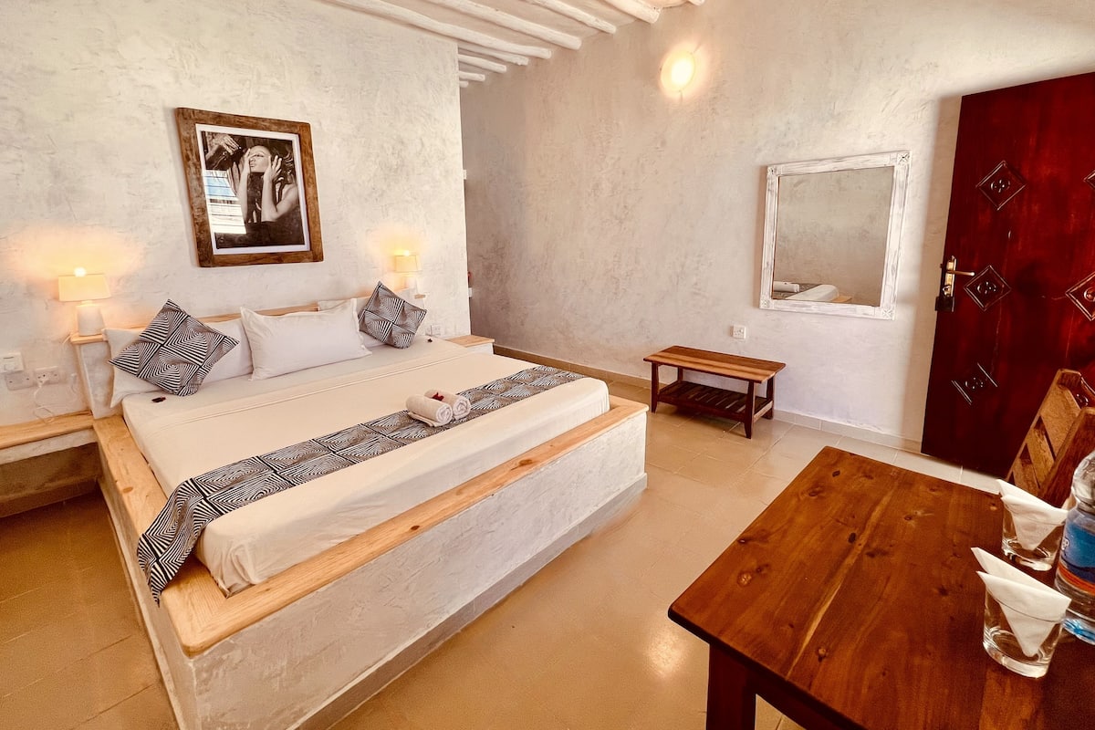 Un dormitorio con una cama, lámparas de noche, un banco de madera, un espejo y una puerta.