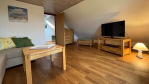 Een knusse woonkamer met een houten vloer, een bank, een tv-meubel en een lamp.