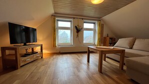 Een gezellige woonkamer met een televisie, houten meubels en een raam met gordijnen.