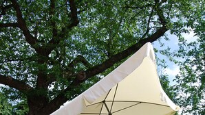 Een terras met een grote parasol, twee rode stoelen en een tafel.