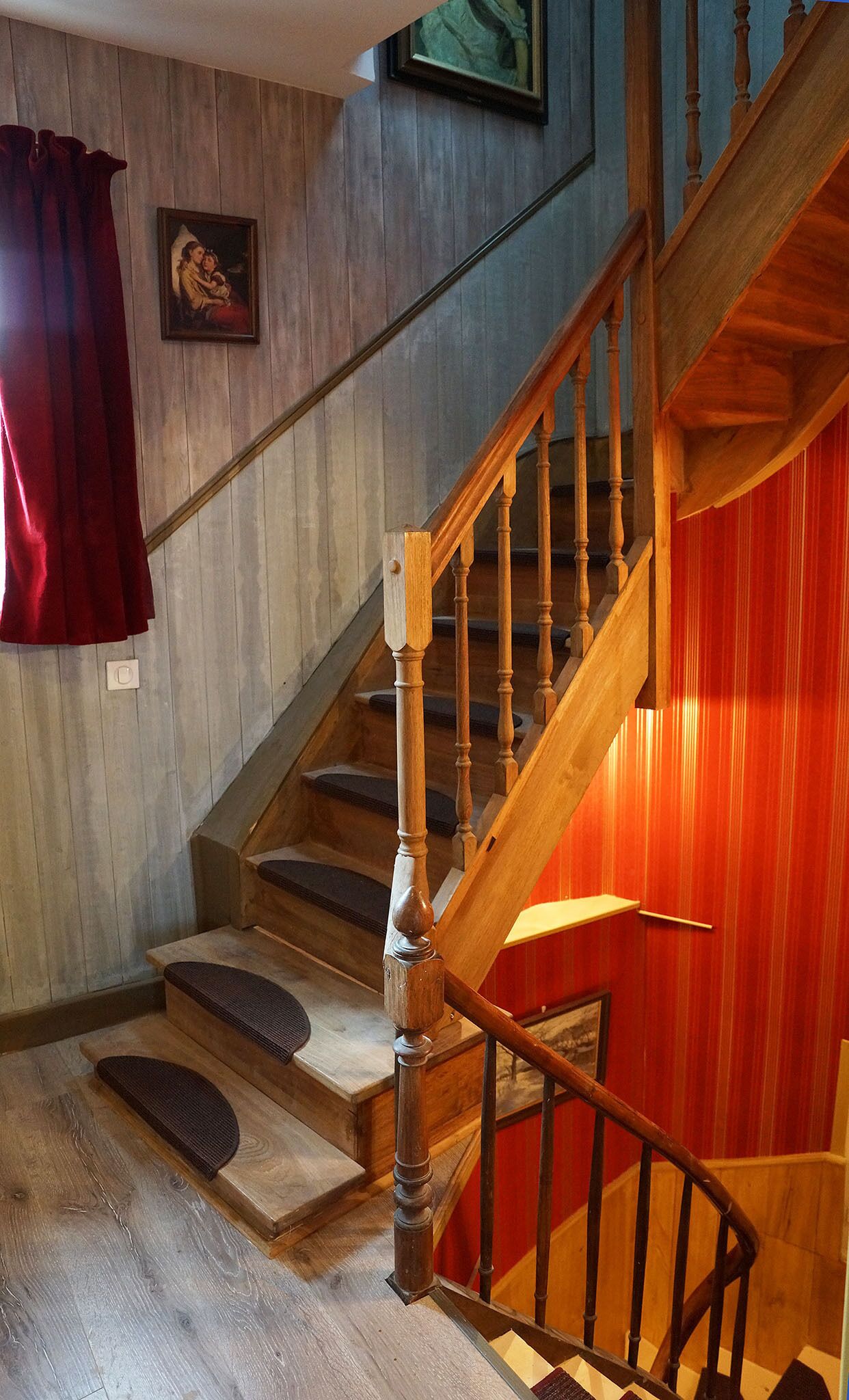 A wooden staircase with a red accent wall, a cushioned landing, and a framed picture on the wall.