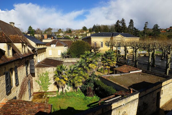 A traditional European town with historic buildings, a central courtyard with palm trees, and a street lined with trees.