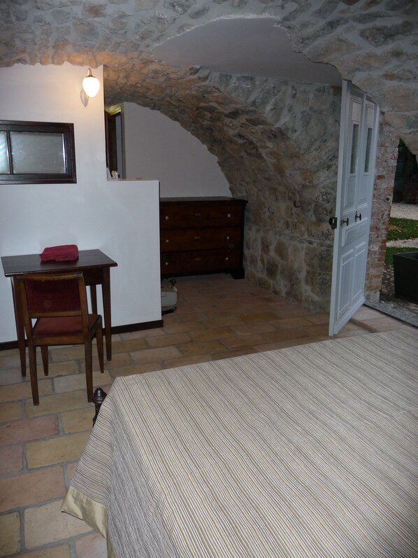 A rustic room with a stone wall, a wooden desk, a chair, a dresser, and a bed. - Le Mas des Bignones, Provençal farmhouse: pool, fenced garden, south of Ardèche (Saint-Alban-Auriolles)