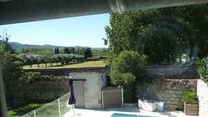 Piscina con vistas a un paisaje rural, muros de piedra y una zona cubierta con una puerta.