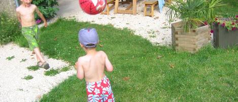 A child playing with a ball in a grassy backyard with a wooden table and benches.