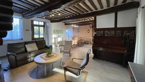 Ein großzügiges Wohnzimmer mit hoher Decke, freiliegenden Balken, einem Kamin und einem Essbereich mit Backsteinwand.