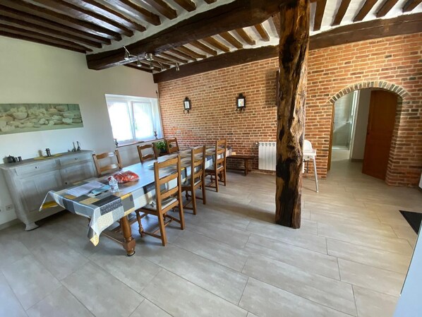 Comedor con una larga mesa, sillas de madera y una pared de ladrillo rústico.