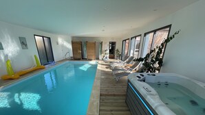 Ein Hallenbad mit Holzterrasse, Liegestühlen und Whirlpool.