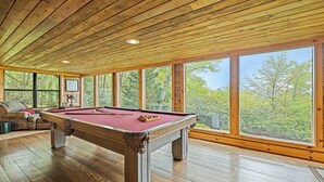 Un tavolo da biliardo in una stanza con pavimenti in legno e ampie finestre.