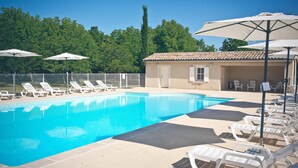 Ein Swimmingpool mit Liegestühlen und Sonnenschirmen, umgeben von einem Zaun und Bäumen.