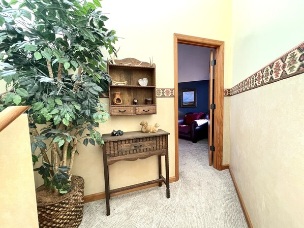 Un pasillo con una consola de madera, una planta en maceta y una puerta que da a una habitación con sofá de cuero y televisor.