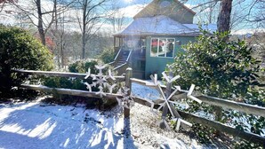 A small cabin with a wooden staircase leading up to a porch, surrounded by snow and trees. - Bear Pause, a perfect family vacation home, minutes from attractions! (Pigeon Forge)