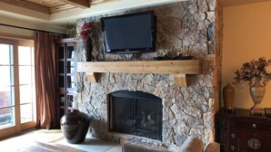 Una sala de estar con chimenea de piedra, televisor montado y un jarrón grande con flores.