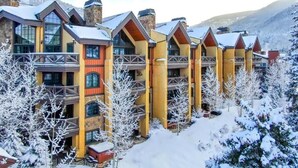 Una hilera de edificios de varios pisos con balcones, frente a un paisaje montañoso nevado.