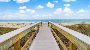 Une promenade en bois menant à une plage, avec un ciel dégagé et quelques nuages.