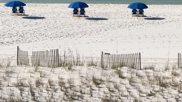 A beach with three blue umbrellas and beach chairs.