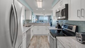 A modern kitchen with stainless steel appliances, white cabinetry, and a large window providing natural light.