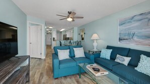 A living room with a blue sofa, a glass coffee table, and a ceiling fan.