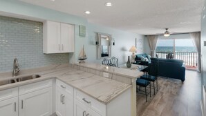 A modern kitchen with white cabinets, a marble countertop, and a view of the balcony.