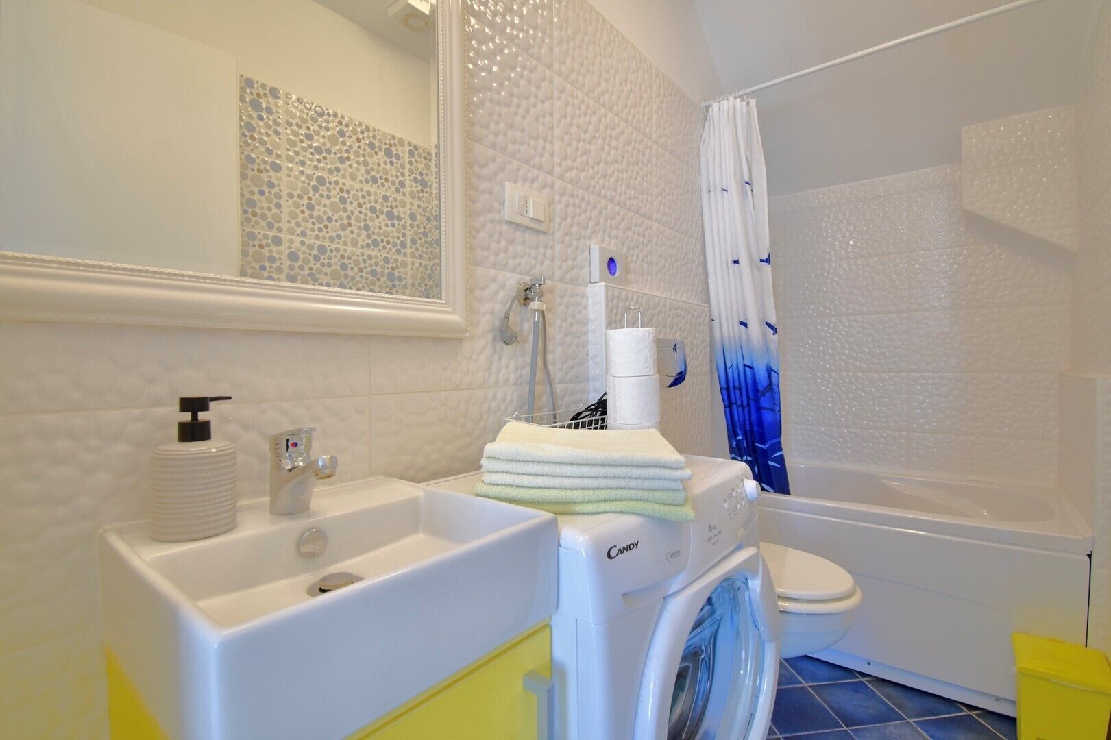 A bathroom with a white sink, a washing machine, a toilet, and a shower curtain.