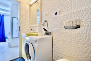 Moderni kylpyhuone, jossa on pesukone, peili ja pyyheteline.