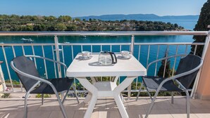 Ein Balkon mit Tisch und Stühlen, der auf ein Gewässer mit Booten und eine entfernte Küste blickt.