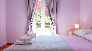 Ein Schlafzimmer mit einem Bett, einem Nachttisch, einer Lampe und Blick ins Grüne.