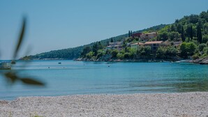 Eine Küstenlandschaft mit Kiesstrand, ruhiger See und Gebäuden an einem Hang.