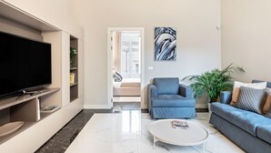 Een moderne woonkamer met een flatscreen-televisie, een salontafel en twee banken. Er is een deur die naar een andere kamer leidt.