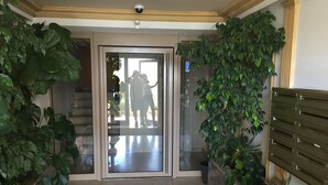 Una hall moderna con una porta in vetro, piante in vaso e una telecamera di sicurezza.