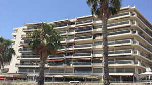 Un edificio a più piani con balconi, un muro di sostegno in pietra e palme.