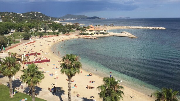 Una spiaggia con acque cristalline, palme e un edificio con tetto rosso.