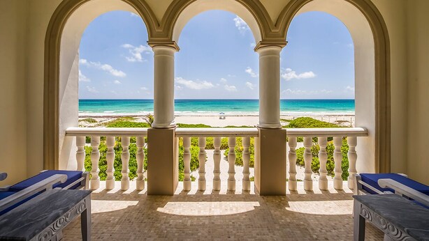 Un balcone con tre archi, vista sulla spiaggia e un tavolo con un cuscino.
