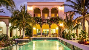 Un hotel con piscina, palme e una zona salotto esterna coperta.