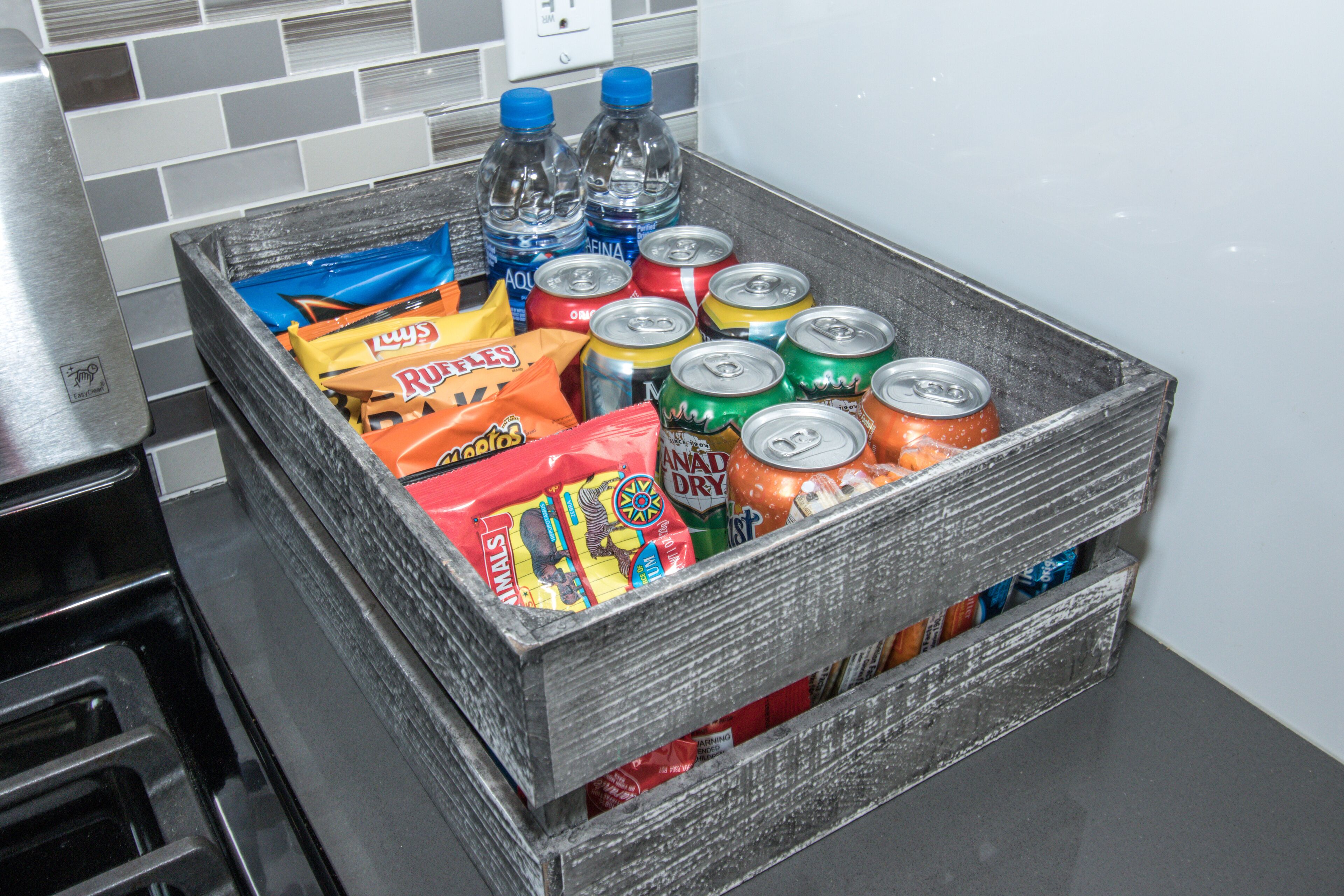 Une caisse en bois remplie de diverses collations et boissons, posée sur un plan de travail de cuisine.