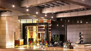 A modern hotel lobby with a reception desk, seating area, and a large window overlooking the street.