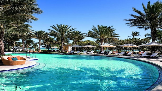 A clear blue pool surrounded by palm trees and lounge chairs.