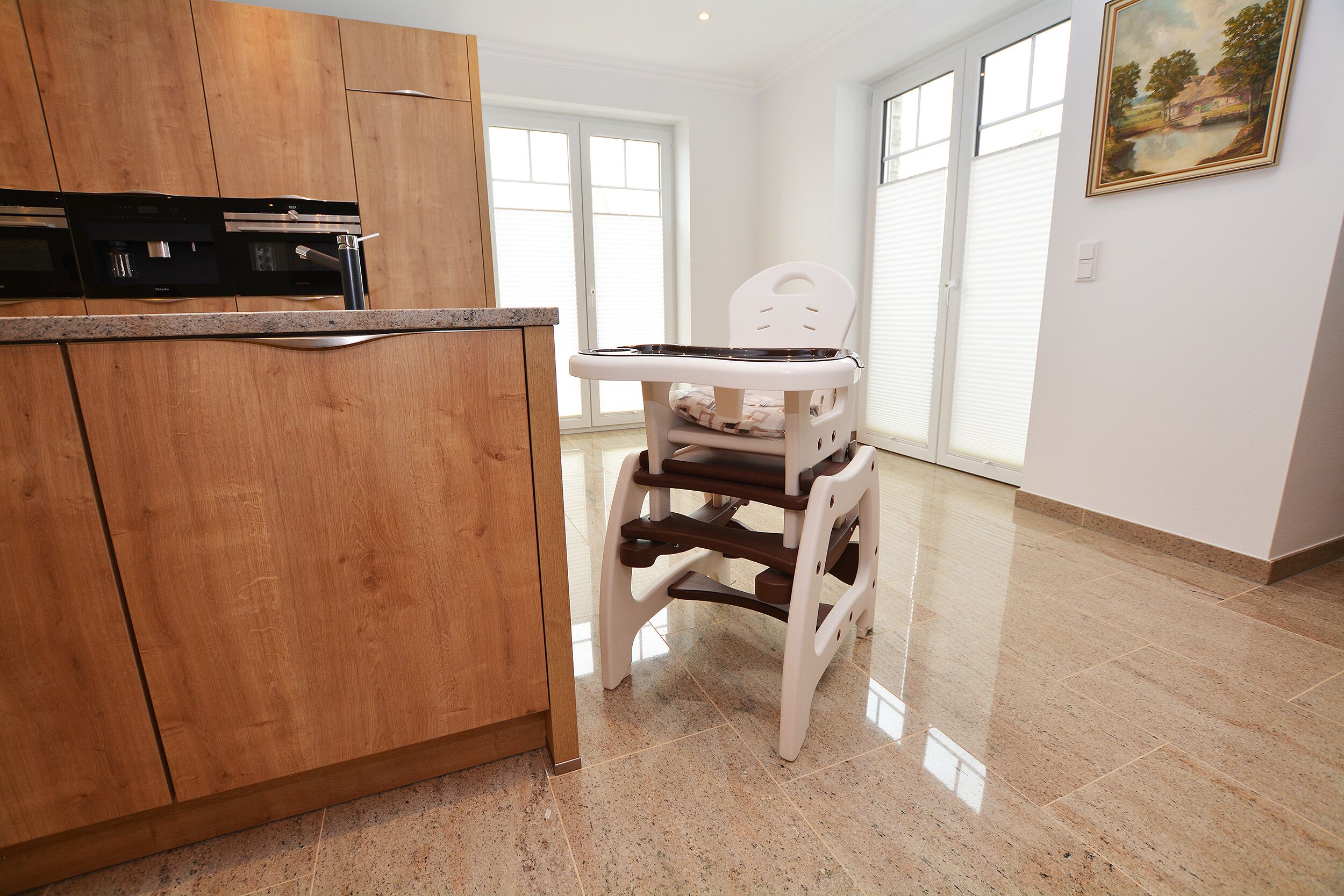Cozinha com armários de madeira, forno embutido e cadeira alta para criança.