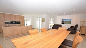 Eine moderne Küche mit eingebauten Geräten, ein Essbereich mit Holztisch und -stühlen sowie ein Wohnzimmer mit Sofa und einem Bild an der Wand.