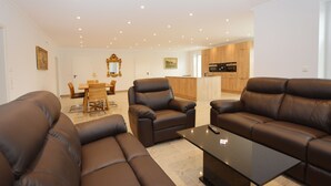 Ein modernes Wohnzimmer mit Ledersofas, einem Glastisch und einem Essbereich mit Holztischen und -stühlen.